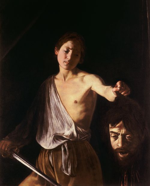 A young man holds a sword and a severed head, standing against a dark background.